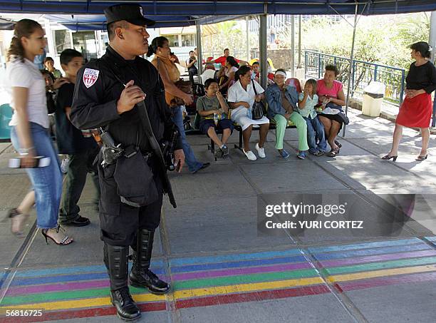San Salvador, EL SALVADOR: Un agente de la policia antimotines monta guardia frente a un grupo de personas que esperan pasar consulta en el Hospital...