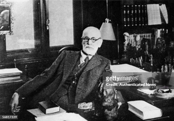 Portrait of Austrian psychologist Sigmund Freud as he sits behind his desk in his study, Vienna, Austria, 1930s. The office is filled with figurines...