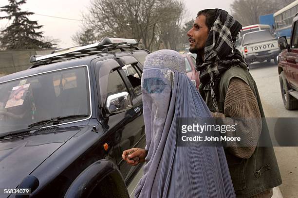 An Afghan woman, covered in a traditional "burqua," leads her blind husband towards an expensive SUV while begging for alms February 12, 2006 in the...