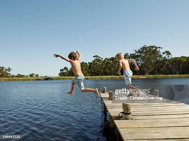 2 boys jumping into the water from a jetty - group-of-friends-jumping-off-dock-into-lake stock pictures, royalty-free photos & images