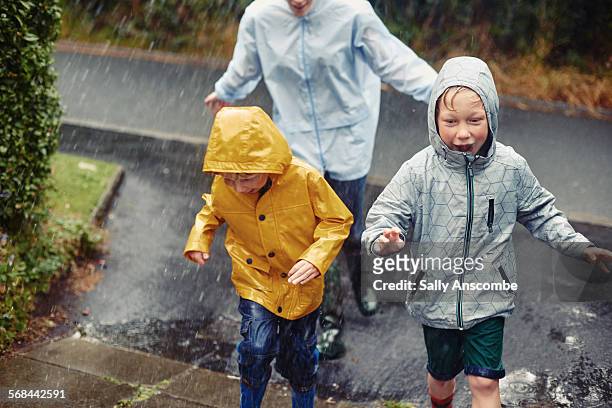 family running home in the rain - raincoat stock-fotos und bilder