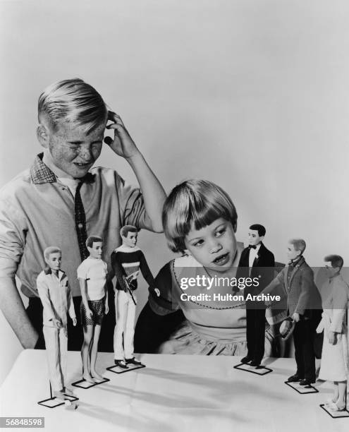 Young boy looks on and scratches his head in confusion as a younger girl inspects the new line of 'Ken' dolls from Mattel, 1961. Ken, whose last name...