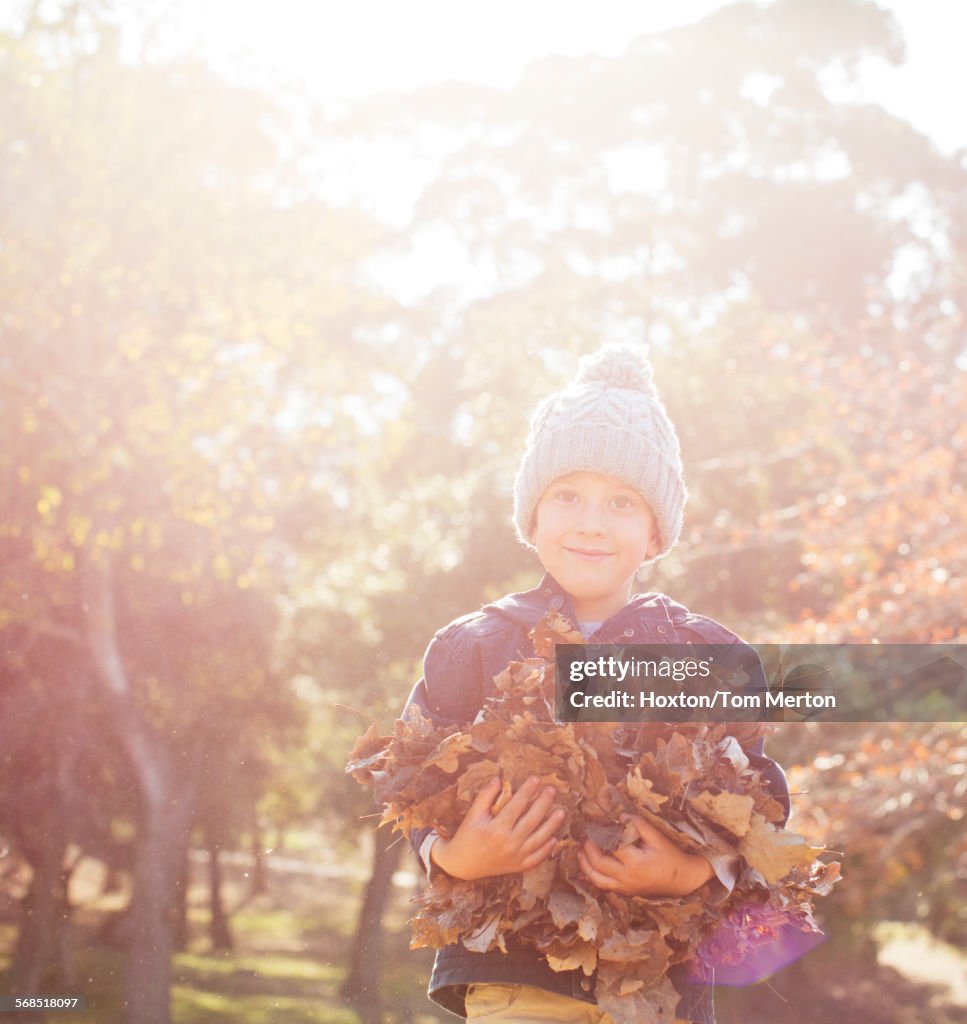 Portrait smiling boy holding bunch of autumn leaves