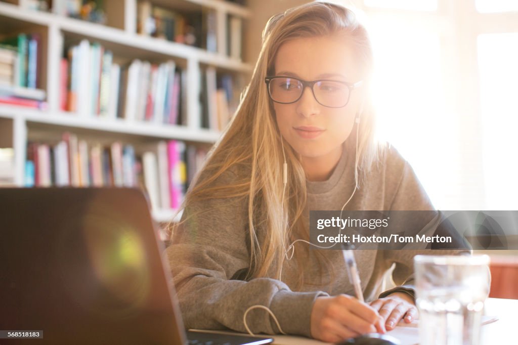 Teenager-Mädchen mit Kopfhörern macht Hausaufgaben mit Laptop