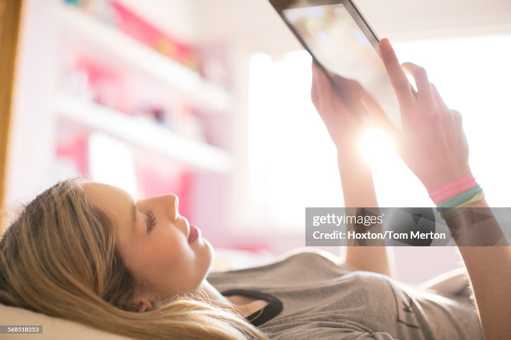 Teenage girl using digital tablet in sunny bedroom