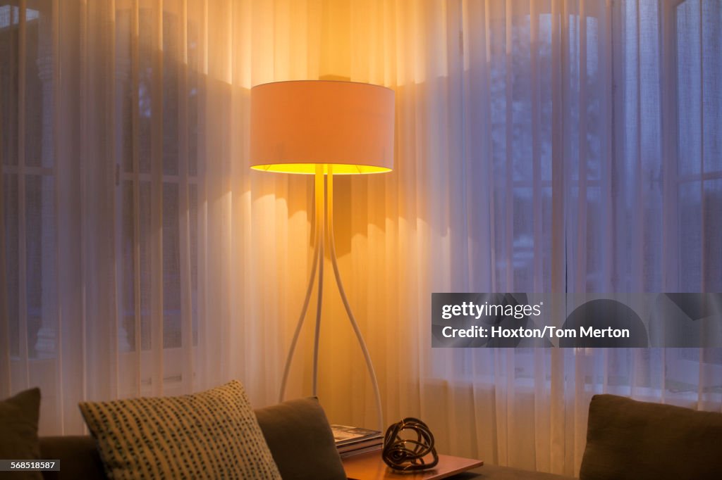 Illuminated floor lamp at window with sheer curtains