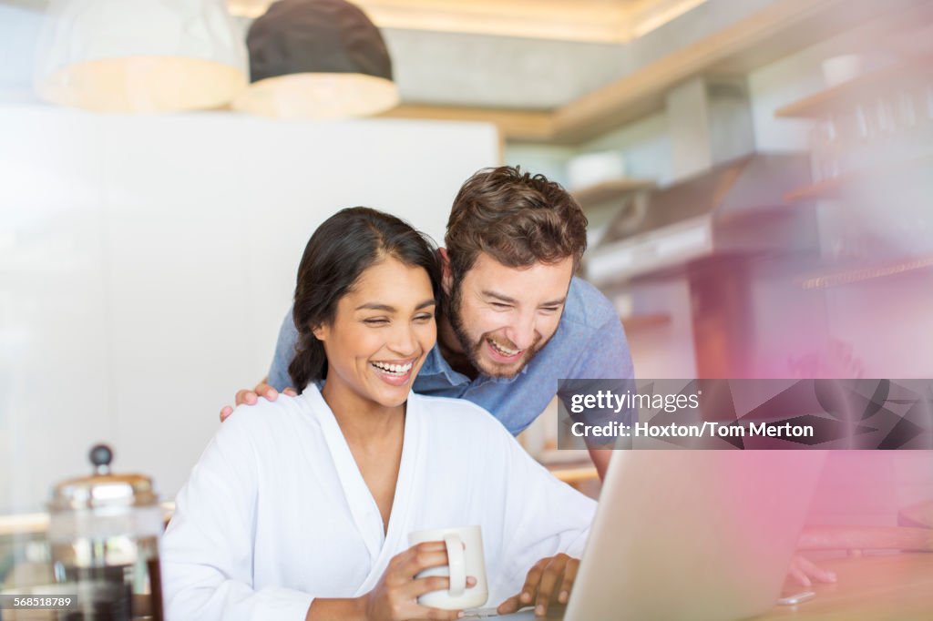 Laughing couple drinking coffee and using laptop