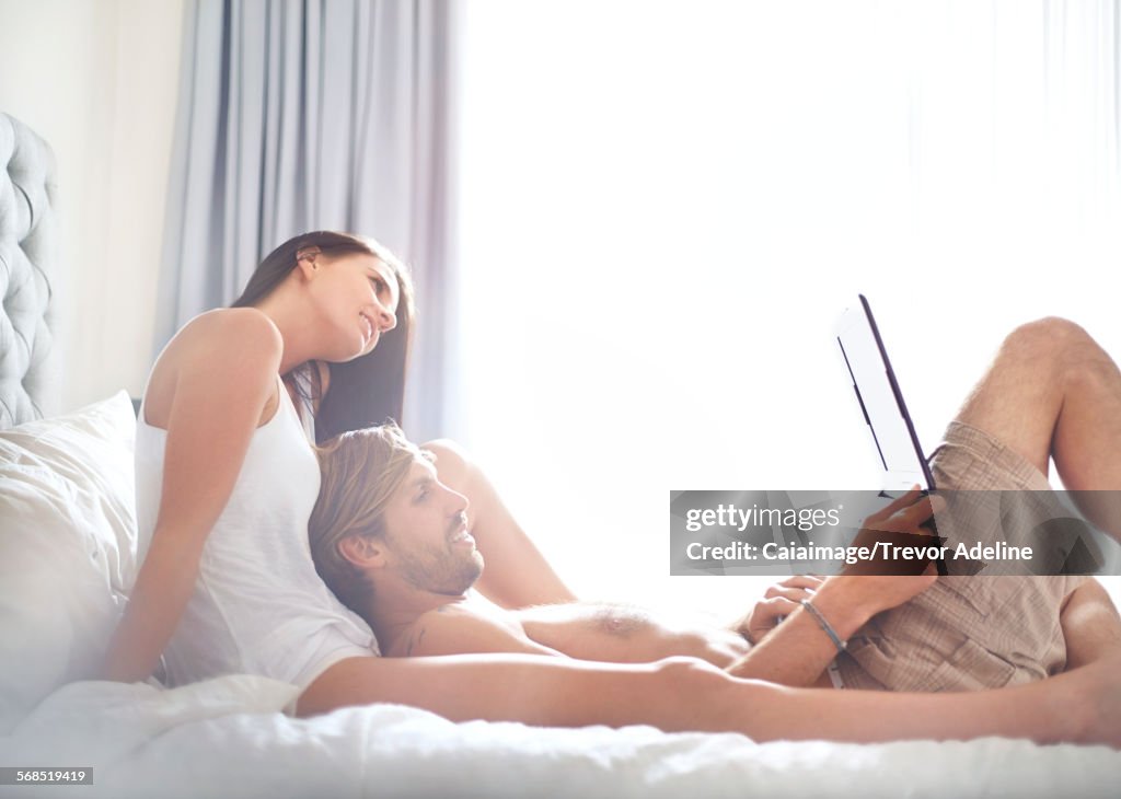 Casual couple relaxing with laptop on bed