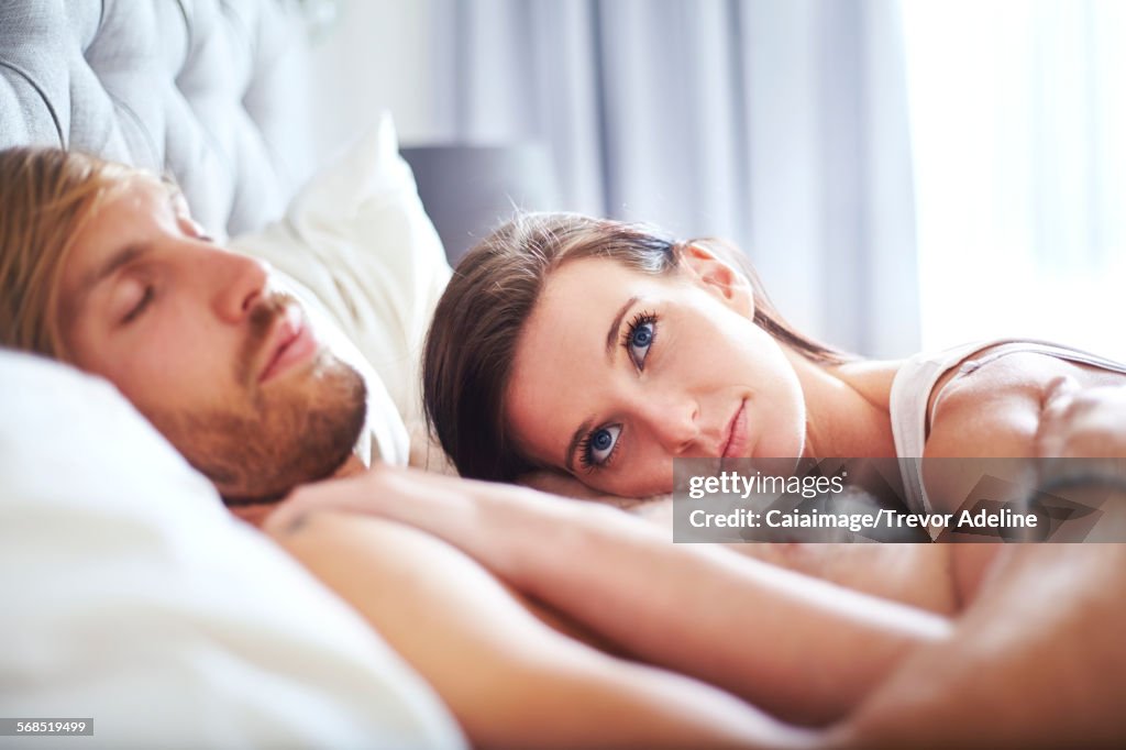 Pensive woman laying on sleeping man on bed