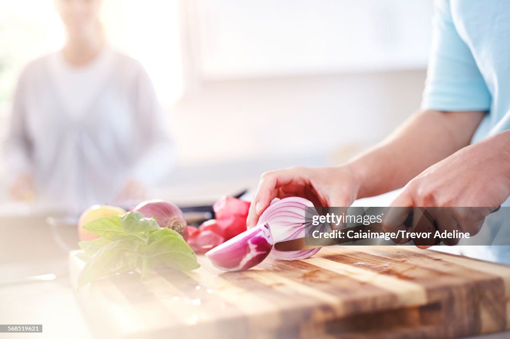 Woman slicing red onion on cutting board in kitchen