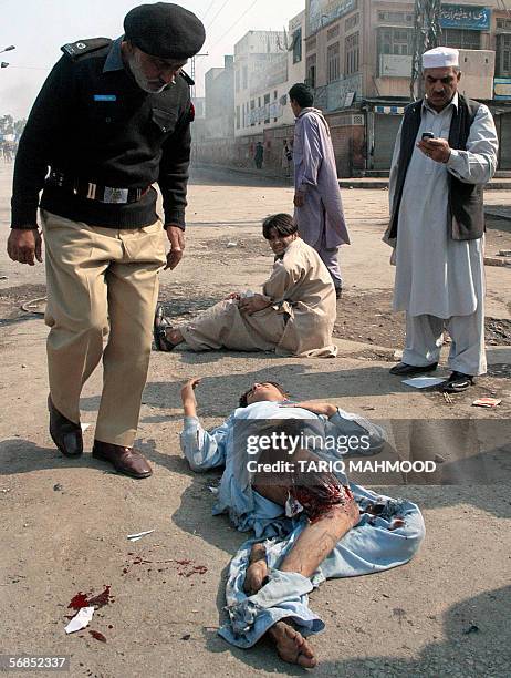 Pakistani policman inspects an injured man after a protest against the publication of cartoons of Prophet Mohammed in Peshawar, 15 February 2006....