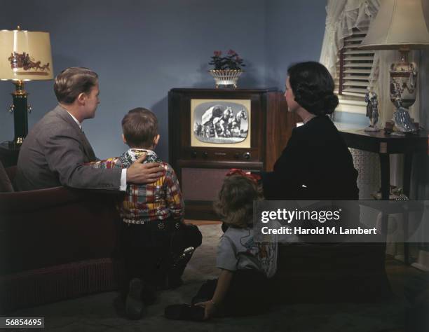 Young family watching a covered wagon on television, 1950. The children are wearing cowboy style outfits in keeping with the programme.