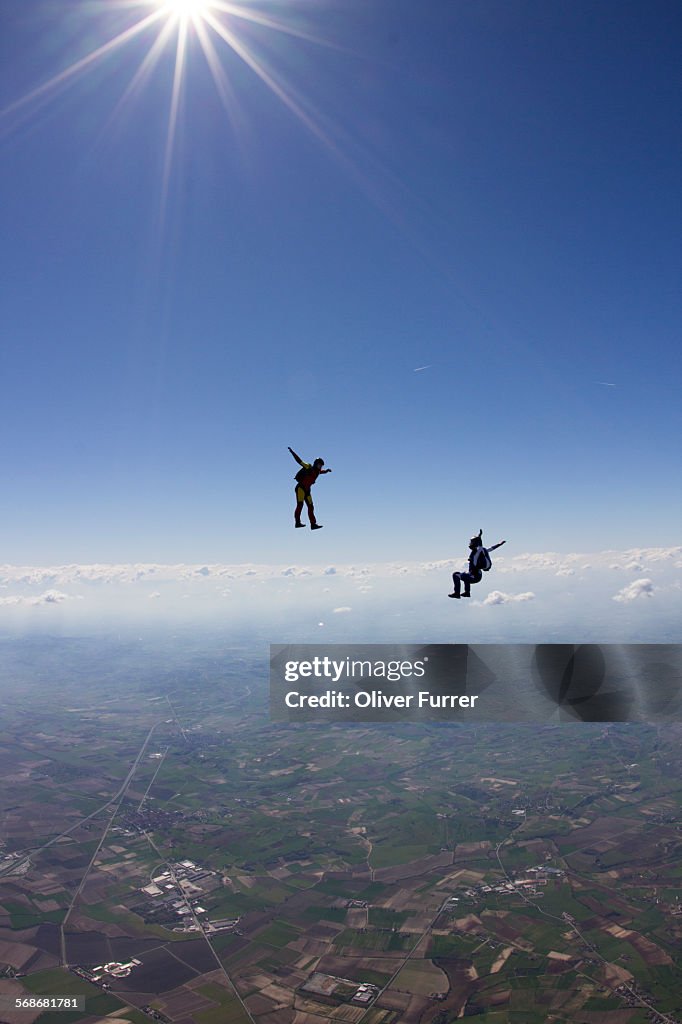 Two skydivers are flying together in the blue sky