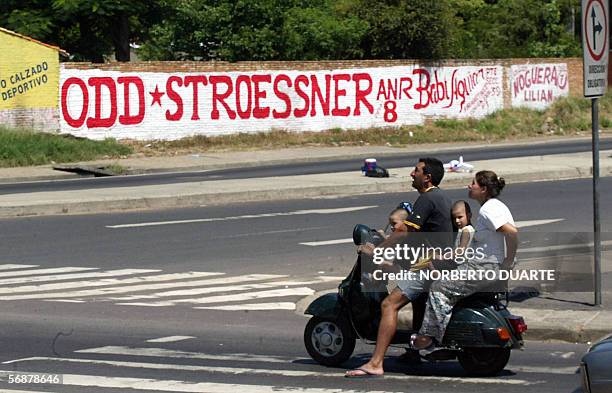 Una familia en motocicleta aguarda para cruzar el 18 de febrero de 2006, en Asuncion, frente a un cartel del empresario Osvaldo Dominguez Dibb -nieto...