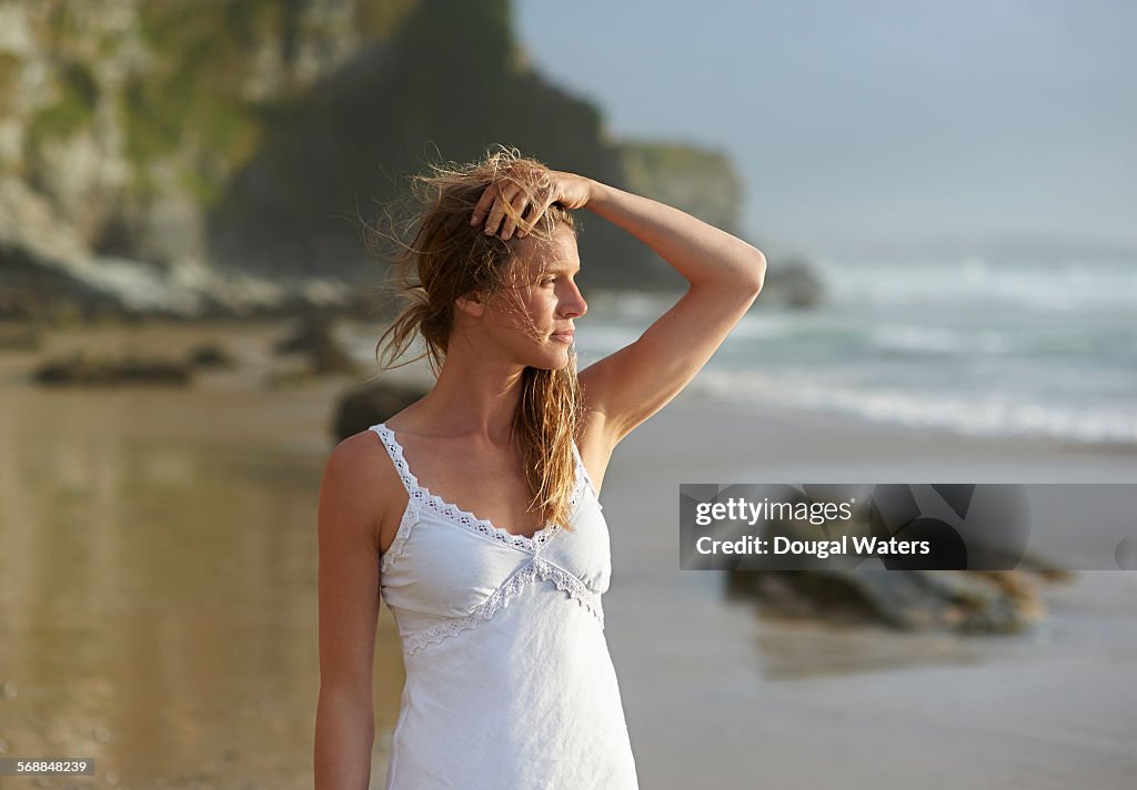 Woman in white looking out to sea from beach.