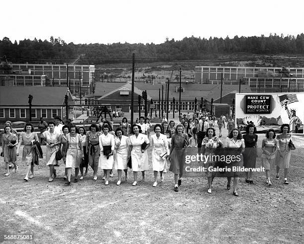 Shift change at the Y-12 uranium enrichment facility in Oak Ridge. 1944. Notice the billboard: "Make CEW count Continue to protect project...