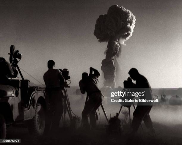 Government filmmakers document an atomic bomb explosion at the test site in Nevada. 1957. A Jeep has been equipped with a movie camera and is not far...