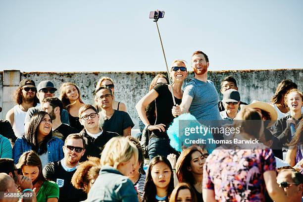 couple in crowd in stadium using selfie stick - monopod stock pictures, royalty-free photos & images