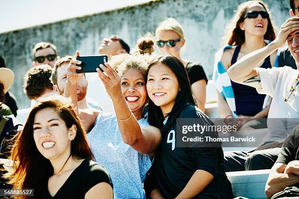 female friends at soccer match taking selfie - voetbalcompetitie sportevenement stockfoto's en -beelden