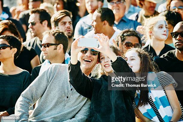 father and daughters taking selfie in stadium - avvenimento sportivo foto e immagini stock