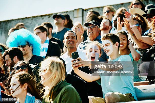 young couple at soccer match taking selfie - voetbalcompetitie sportevenement stockfoto's en -beelden