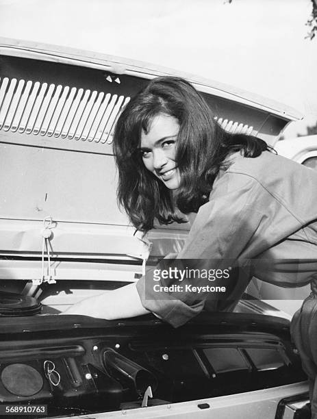 Actress Marie Versini working under the hood of car, after winning a competition by changing a spark plug in 24 seconds, on the set of the film 'The...
