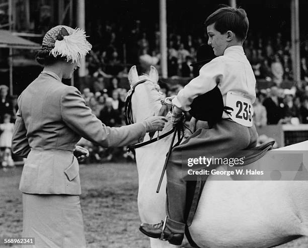 Queen Elizabeth II presenting the first prize rosette to 7 year old David Mayers at a children's leading rein pony class, at Richmond Royal Horse...