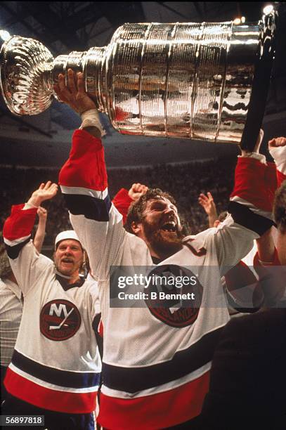 Canadian professional hockey player Denis Potvin of the New York Islanders hoists the Stanley Cup over his head as he celebrates their championship...