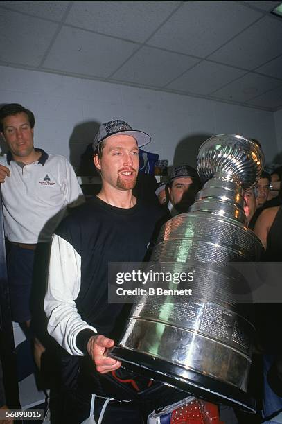 Canadian professional hockey player Patrick Roy of the Colorado Avalanche hoists the Stanley Cup over his head in the dressing room as he celebrates...