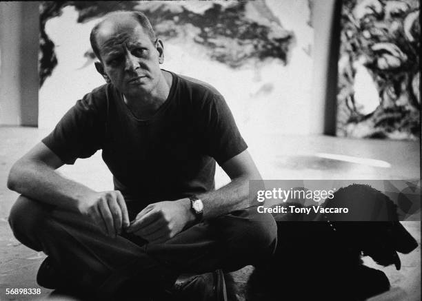 American abstract expressionist painter Jackson Pollock sits with a black dog, possibly a curly coated retriever, in his studio at 'The Springs,'...
