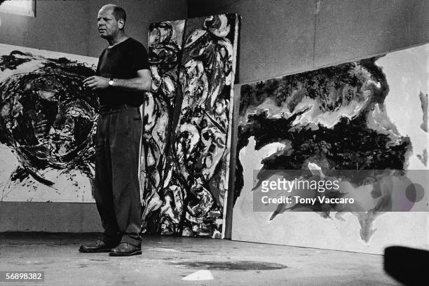 American abstract expressionist painter Jackson Pollock stands amid some large paintings in his studio at 'The Springs,' East Hampton, New York,...