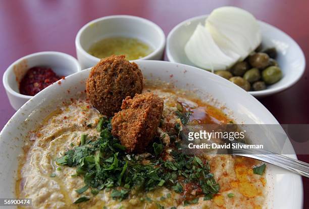 Bowl of hummous is served with olive oil, falafel balls and sprinkled with chopped parsley alongside olives, a fresh onion, chili and lemon juice and...