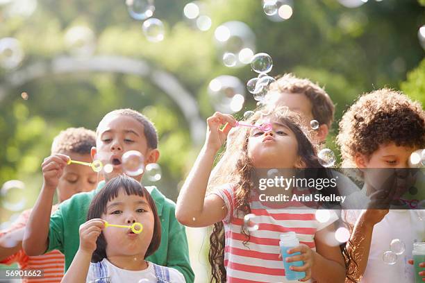children outdoors blowing bubbles - jugar fotografías e imágenes de stock
