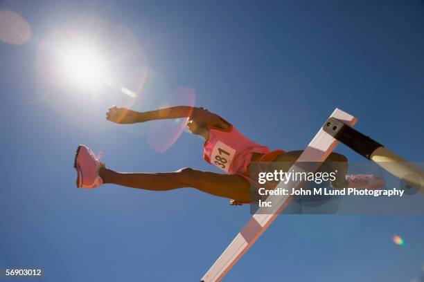 female track participant jumping over hurdle - leichtathletik stock-fotos und bilder