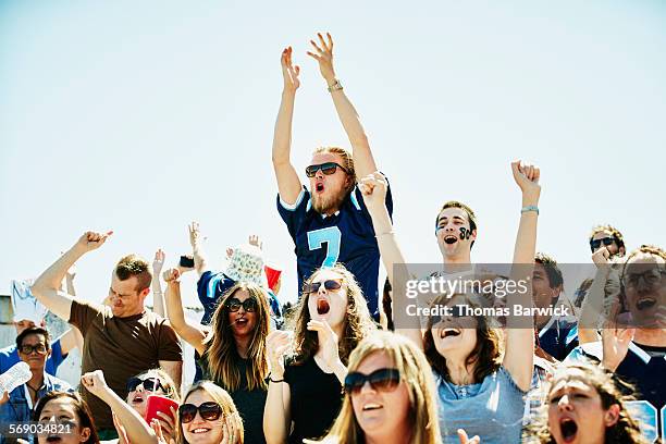 fan jumping above celebrating crowd in stadium - american football sport stock-fotos und bilder