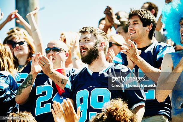 smiling man in crowd of celebrating football fans - football jersey stock pictures, royalty-free photos & images