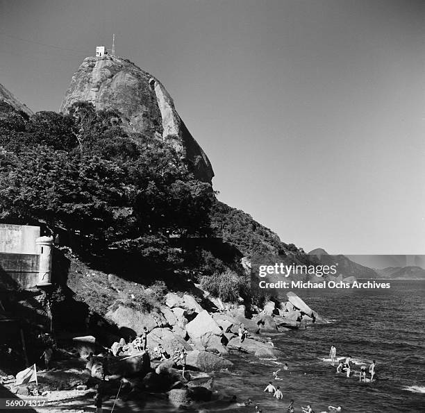 View of the cable car on Sugarloaf Mountain as people swim in the ocean in Rio de Janeiro, Brazil.
