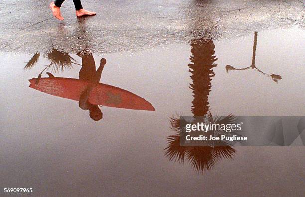 Surfer is reflected in a rain puddle as he walks towards Silver Strand Beach in Oxnard Wednesday. A light misty rain fell most of the day, but that...