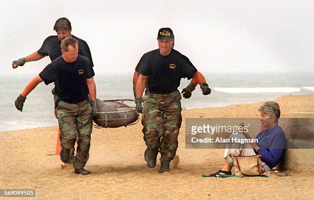 Ann Welp, right, Thousand Oaks reads a magazine at Surfers Point in Ventura as members of Oxnard Police Dept. SWAT team carry a 185 lb. Dummy along...