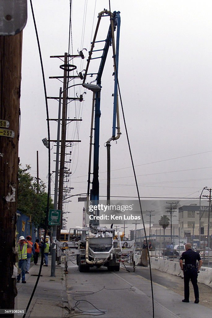 LAPD officer, rt., stands near tangle of fallen eletrical line near concrete pumping truck which tou