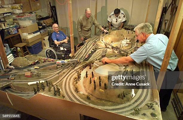 Four members of the Gold Coast Modular Railroad Club play with a train set that lowers from the ceiling of the garage of Wjillis Naysmith's home in...