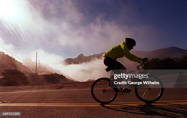 Bicyclist breaks through the fog as he nears a summit on Mulholland Highway west of Las Virgenes Rd. Early this morning.