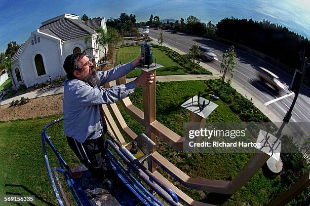 With the synagogue in the backround, left, Rabbi David Eliezrie places a light on top of the permanent menorah that stands in front of the...