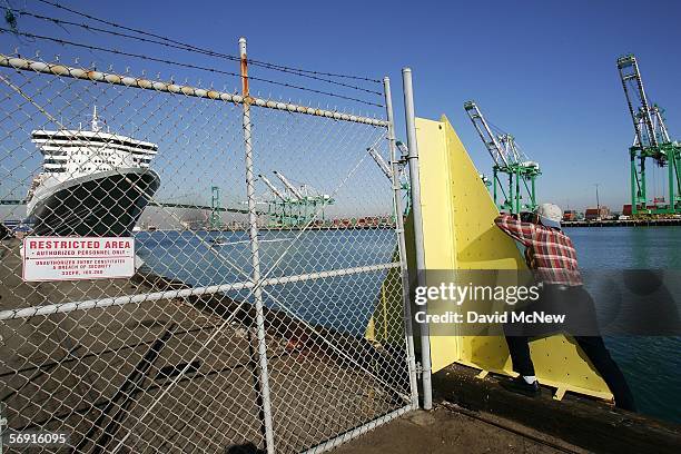 Man reaches around a fence barrier to photograph the Queen Mary 2 Commodore Warwick cruise ship on its maiden call to the Port of Los Angeles...