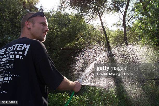 Passerby Tim Haendiges of Woodland Hills, uses a garden hose to wet the vegetation behind the home on the 23200 block of Mulholland Highway in...