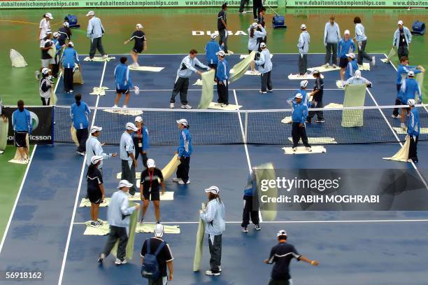 Dubai, UNITED ARAB EMIRATES: Staff of the Dubai Open tournament dry the central tennis court after heavy rain in the oil-rich Gulf emirate, 23...