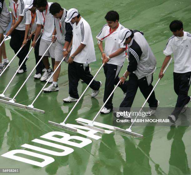 Dubai, UNITED ARAB EMIRATES: Staff of the Dubai Open tournament dry the central tennis court after heavy rain in the oil-rich Gulf emirate, 23...