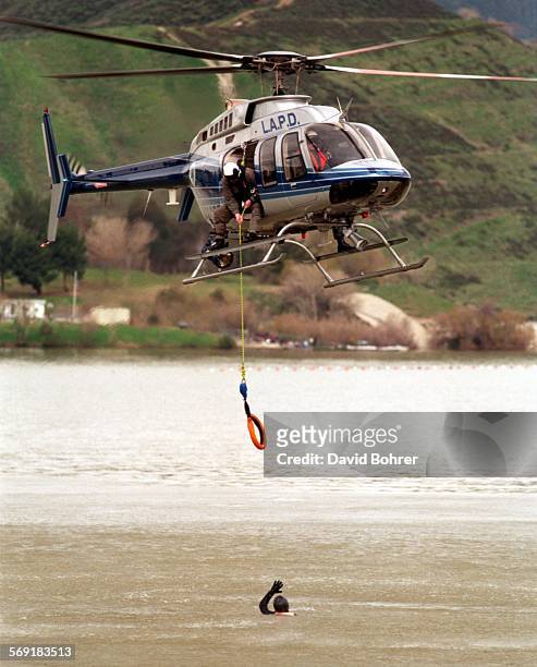 An LAPD helicopter lowers a line to the water for a wetsuitdonned officer during a simulated rescue while training at Castaic Lake. Using the new,...