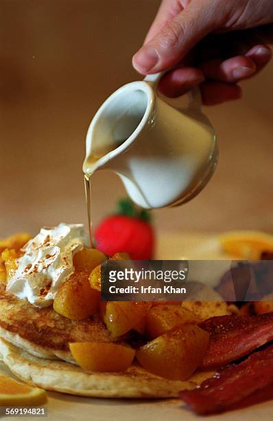 Peach pancakes topped with whipped cream, sprinkled ground cinammon and maple syrup is served with seasoned potatos, bacon and strawberries served at...