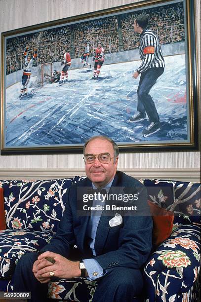 Portrait of General Manager of the New York Islanders Bill Torrey, a cigar in his hand, as he sits on a sofa underneath a painting that depicts Bobby...